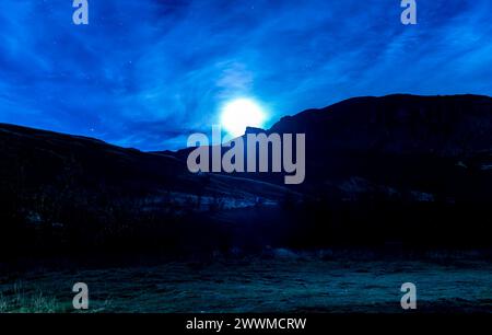 Une lune brille brillamment dans le ciel au-dessus d'une chaîne de montagnes. La scène est paisible et sereine, avec la lune projetant une douce lueur sur le paysage Banque D'Images