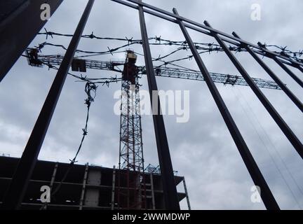 Chantier de construction inachevé clôturé avec du fil de fer barbelé et une grue de construction floue en arrière-plan Banque D'Images