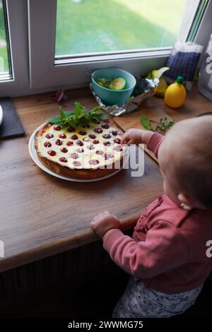 Une petite fille mignonne essaie un gâteau aux baies pour son premier anniversaire Banque D'Images