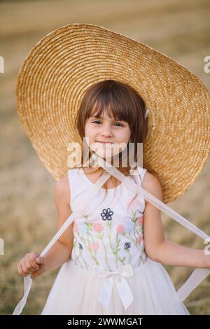 Jolie petite fille en robe d'été et chapeau de paille posant en plein air Banque D'Images