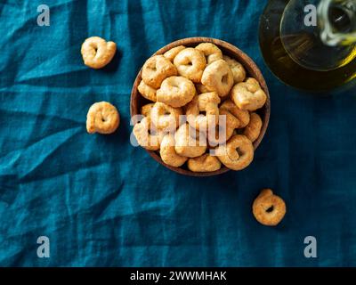 Taralli ou tarallini de snack italien traditionnel dans un bol en bois sur fond de serviette en lin bleu foncé. Plan rustique de taralli apéritif avec espace de copie. Vue de dessus ou pose à plat. Banque D'Images