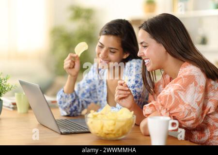 Deux femmes à la maison mangeant des bateaux de pommes de terre regardant le film sur ordinateur portable Banque D'Images