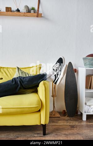 plan recadré de jambes d'homme dans des baskets noires couchées pour croiser sur un canapé jaune dans le salon Banque D'Images
