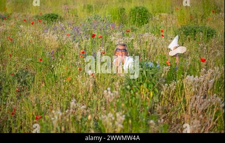 fröhliche Junge Frau mit Sonnenbrille liegt in einer Blumenwiese *** jeune femme joyeuse avec des lunettes de soleil se trouve dans un pré de fleurs Banque D'Images