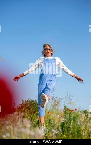 fröhliche Junge Frau mit Sonnenbrille im Mohnfeld *** jeune femme joyeuse avec des lunettes de soleil dans un champ de coquelicots Banque D'Images