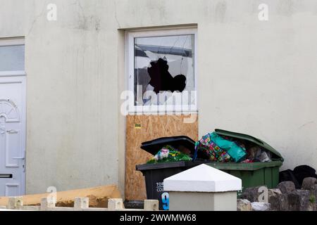 Fenêtre brisée à l'extérieur de la façade d'une maison résidentielle avec beaucoup de déchets dehors Banque D'Images