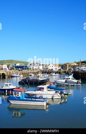 Vue des bateaux de pêche traditionnels amarrés dans le port à marée basse avec la ville et la campagne à l'arrière, West Bay, Dorset, Royaume-Uni, Europe. Banque D'Images