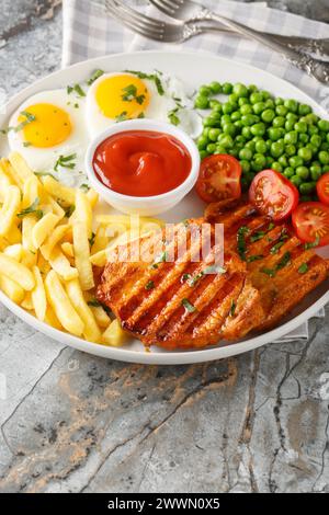 Steak grillé avec petits pois, oeuf frit, frites, tomates et sauce gros plan dans une assiette sur la table. Vertical Banque D'Images