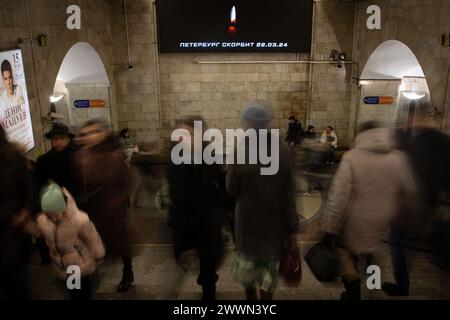 Passants dans un passage de métro sur fond d’écran avec l’image d’une bougie allumée et l’inscription « Petersburg Mourns » pour les victimes de l’attentat terroriste à la mairie de Crocus, organisé à Petersburg. La Russie pleure les victimes de l'attentat terroriste à la mairie de Crocus à Moscou. Le 24 mars est devenu un jour de deuil national dans le pays. Les gens de toute la Russie apportent des fleurs aux mémoriaux spontanés pour déposer des fleurs et honorer la mémoire des victimes de l'attaque terroriste. Selon les dernières données du comité d'enquête de la Russie, 137 décès sont connus Banque D'Images