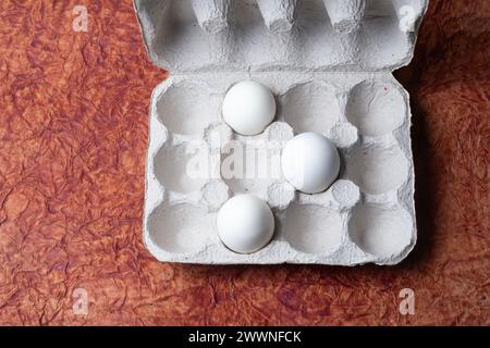 Oeufs blancs dans une boîte en carton sur un fond de papier texturé brun. Vue de dessus. Banque D'Images
