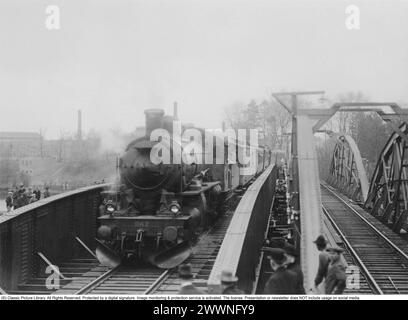 Histoire ferroviaire. La première locomotive à vapeur et les premiers wagons traversent le nouveau pont ferroviaire sur la voie navigable Nissan à Halmstad. Le nouveau pont en acier remplace l'ancien sur la droite. Les gens se sont rassemblés pour regarder passer le premier train. Avril 1928 Banque D'Images