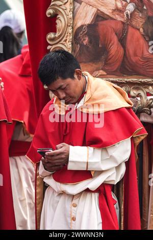 Antigua, Guatemala. 24 mars 2024. Un pénitent catholique voit son téléphone portable avant de diriger une procession massive lors de la procession du dimanche des Rameaux la Reseña depuis la Parroquia San Sebastián la Merced marquant le début de la semaine Sainte, le 24 mars 2024 à Antigua, Guatemala. Les processions opulentes, les algèbres détaillées et les traditions séculaires attirent plus d'un million de personnes dans l'ancienne capitale. Crédit : Richard Ellis/Richard Ellis/Alamy Live News Banque D'Images