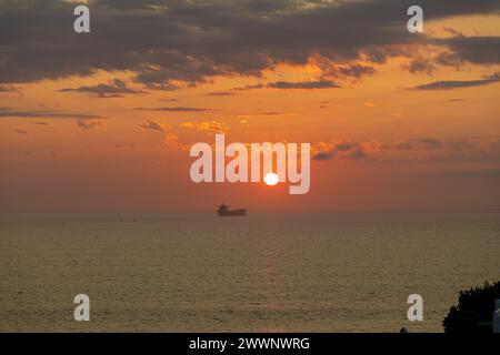 Navire sur l'océan pendant un coucher de soleil incandescent avec un soleil brûlant chaud et des nuages dans le ciel. Banque D'Images