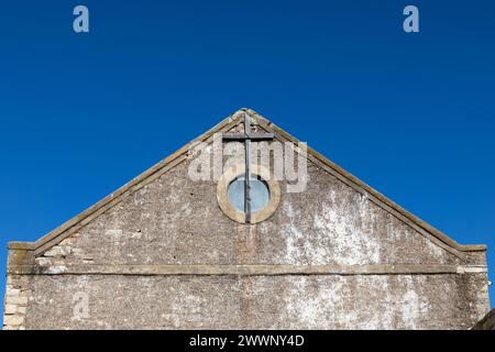 Extrémité de pignon d'une ancienne église abandonnée avec une fenêtre circulaire et une croix en bois attachée au mur. Banque D'Images