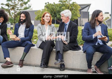 Des gens d'affaires de différentes ethnies et âges mangeant et discutant ensemble en plein air à la pause déjeuner - concept de réunion et d'entreprise Banque D'Images