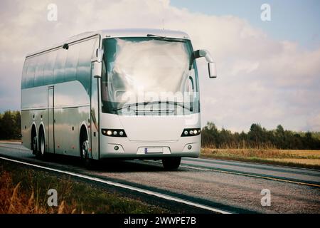 Bus argenté voyageant le long de l'autoroute à travers le paysage rural dans la lumière automnale. Banque D'Images