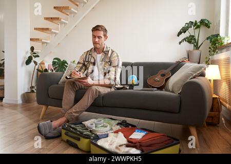 Portrait d'un jeune homme faisant l'emballage pour un voyage, partant en vacances, mettant des vêtements à l'intérieur de la valise, se préparant pour les vacances Banque D'Images
