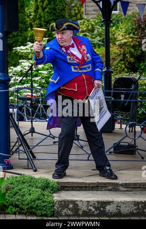 Crieur de ville masculin et chasseur (vêtements de livrée du crieur rouge bleu) faisant une proclamation publique bruyante et bruyante - Ilkley, West Yorkshire, Angleterre Royaume-Uni. Banque D'Images