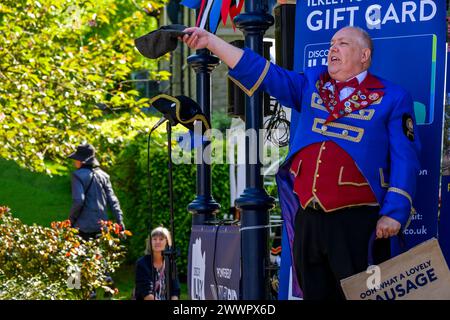 Crieur de ville masculin ou chasseur (costume de crieur rouge bleu, chapeau tricorne, tenant une casquette plate) faisant une annonce forte - Ilkley, West Yorkshire, Angleterre Royaume-Uni. Banque D'Images