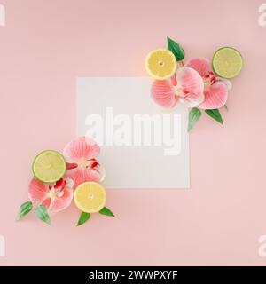 Mise en page tendance faite avec des fleurs d'orchidée, citron vert, feuilles vertes et espace de copie de note de carte de papier sur fond rose clair. Concept alimentaire créatif. Banque D'Images