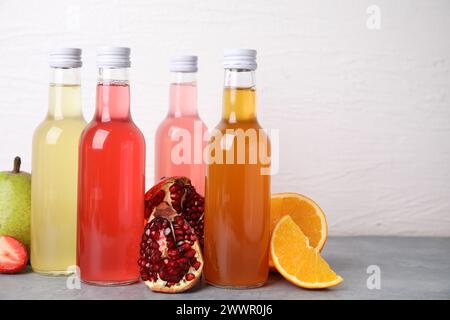 Délicieux kombucha dans des bouteilles en verre et des fruits frais sur une table grise sur fond blanc Banque D'Images