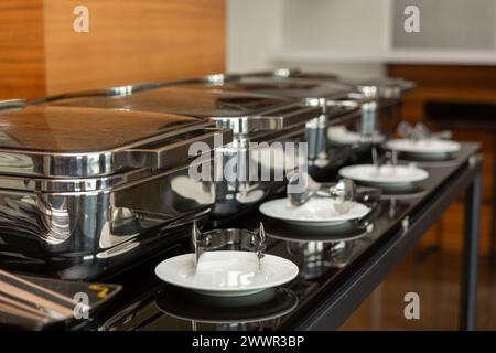 Rangée de plats buffet fermés dans la salle de banquet. Plat à frotter prêt pour le service en acier inoxydable au buffet. Banque D'Images