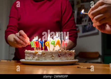 mains avec allumettes allumant des bougies vax sur le gâteau d'anniversaire Banque D'Images