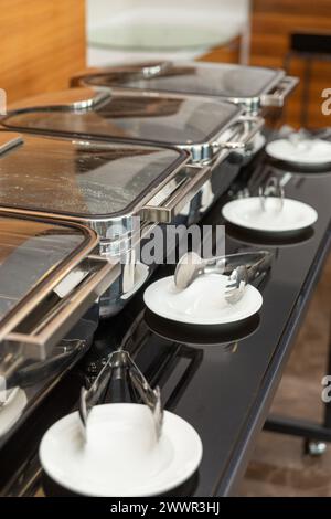 Rangée de plats buffet fermés dans la salle de banquet. Plat à frotter prêt pour le service en acier inoxydable au buffet. Banque D'Images