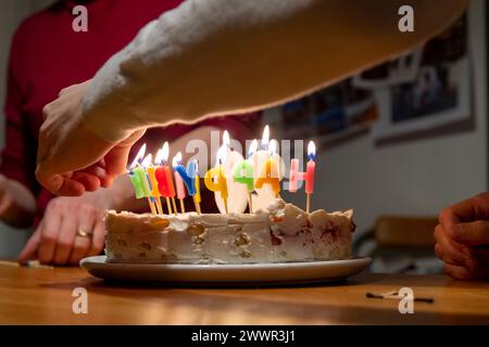 mains avec allumettes allumant des bougies vax sur le gâteau d'anniversaire Banque D'Images