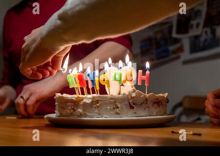 mains avec allumettes allumant des bougies vax sur le gâteau d'anniversaire Banque D'Images