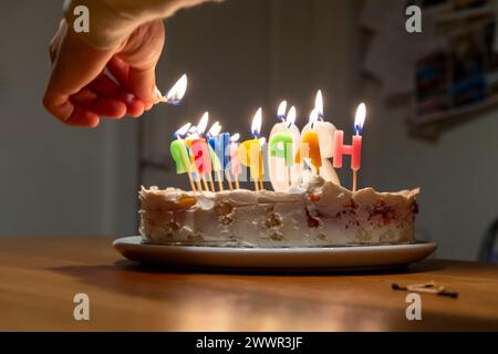 mains avec allumettes allumant des bougies vax sur le gâteau d'anniversaire Banque D'Images