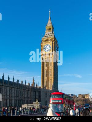 Emblématique bus à impériale rouge passant devant Big Ben et les chambres du Parlement sous un ciel bleu clair à Londres, au Royaume-Uni. Banque D'Images