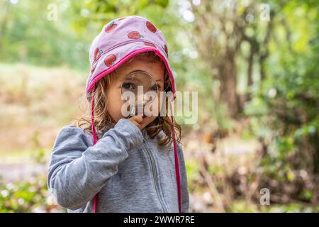 Curieuse fille avec loupe, découvrant les merveilles de la nature. L'esprit curieux brille à travers le jeu d'un enfant dans la forêt, la beauté d'learni Banque D'Images