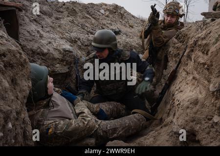 15 mars 2024, Kiev, Ukraine : des stagiaires approchent un soldat potentiellement blessé dans une formation simulant une mission d’évacuation dans la tranchée organisée par la troisième brigade d’assaut séparée dans la région de Kiev. L'Ukraine est confrontée à une pénurie de munitions et de personnel militaire. En plus d’une loi de mobilisation plus sévère en cours, certaines brigades du pays ont choisi une approche plus encourageante pour recruter des personnes sans expérience militaire préalable pour rejoindre l’armée. La troisième brigade d'assaut offre un cours de formation gratuit de 7 jours pour permettre aux participants d'avoir un avant-goût du tra militaire Banque D'Images