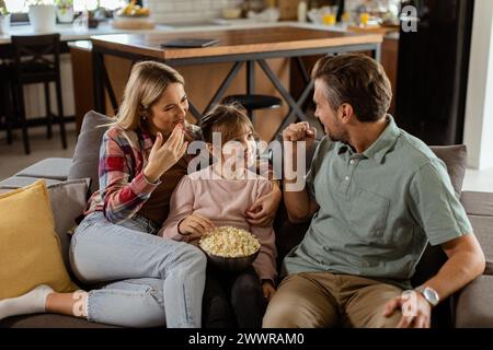 Un joyeux salon familial sur le canapé, s'engageant dans une conversation ludique avec un bol de pop-corn Banque D'Images