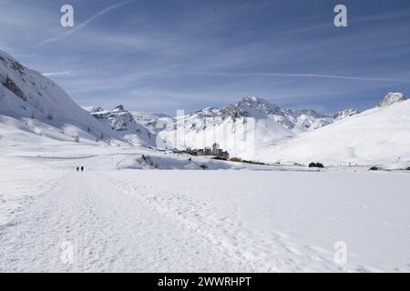 Les gens traversent le lac gelé de Tignes, en France, vers le quartier Val Claret dominé par les sommets de la petite Balme, de la Grande Motte et de la Grande casse. Banque D'Images