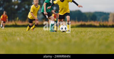 Les garçons des équipes de football donnent un coup de pied au ballon sur gazon. Enfants jouant au football. Ballon dribble de joueur de football junior et rivaliser avec Defender Banque D'Images