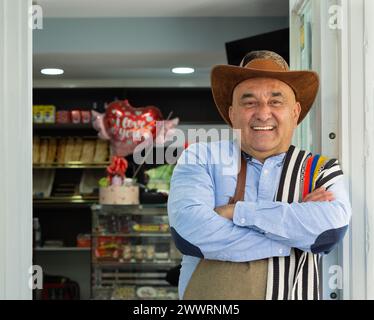 Entrepreneur colombien penché à l'entrée de son entreprise avec un sourire sur le visage Banque D'Images