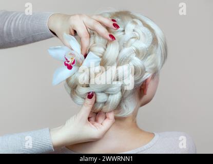 Belle fille aux cheveux blonds, coiffeuse tisse un gros plan de tresse, dans un salon de beauté. Soins capillaires professionnels et création de coiffures. Banque D'Images