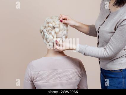 Belle fille aux cheveux blonds, coiffeuse tisse un gros plan de tresse, dans un salon de beauté. Soins capillaires professionnels et création de coiffures. Banque D'Images