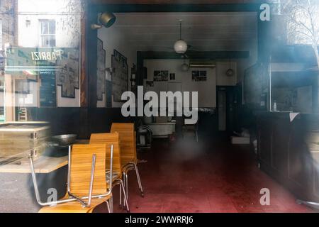 Londres, Royaume-Uni. 19 mars 2024. L'intérieur de Alpino Cafe dans Chapel Market est photographié à travers la fenêtre. Le populaire café britannique-italien servait ses clients à Islington depuis 1959, mais a été forcé par la hausse des loyers et des prix de fermer et de déménager de l'autre côté de la rue avec un nom différent en 2022. Les nouveaux locaux apparaissent reflétés dans la fenêtre des anciens locaux. Crédit : Mark Kerrison/Alamy Live News Banque D'Images