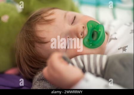 Mignon bébé garçon dort paisiblement avec une sucette, tenant son jouet en peluche préféré, sous la lumière du jour douce. Incarnation tranquillité et innocence Banque D'Images