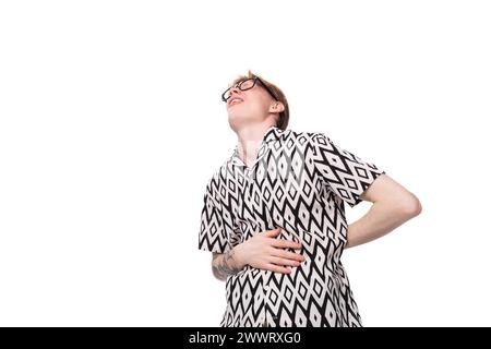 jeune homme optimiste drôle avec les cheveux roux dans des lunettes et une chemise noire et blanche d'été rit à voix haute et ressent des douleurs dans son estomac Banque D'Images