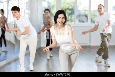 Fille aime la danse active, apprend de nouveaux mouvements, se déplace de manière synchrone avec les participants de la leçon Banque D'Images