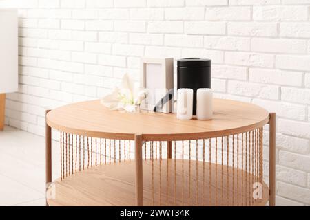 Cadre funéraire vierge, urne mortuaire, bougies et fleur de lys sur une table en bois près d'un mur de briques claires Banque D'Images