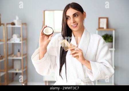 Belle jeune femme avec noix de coco peignant les cheveux dans la salle de bain Banque D'Images