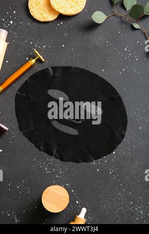 Masque de drap facial avec différents produits cosmétiques et eucalyptus sur fond noir Banque D'Images