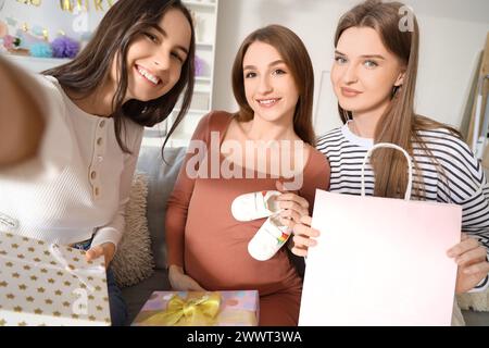 Jeune femme enceinte avec ses amis et cadeaux prenant selfie à la fête de douche de bébé Banque D'Images