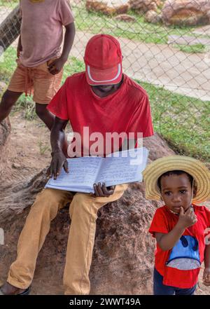 travailleur social africain , lecture d'un livre aux enfants du village , éducation communautaire, plein air retour à l'école à l'ombre de l'arbre, maison s. Banque D'Images