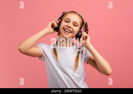 Fille avec des écouteurs appréciant la musique, fond rose Banque D'Images